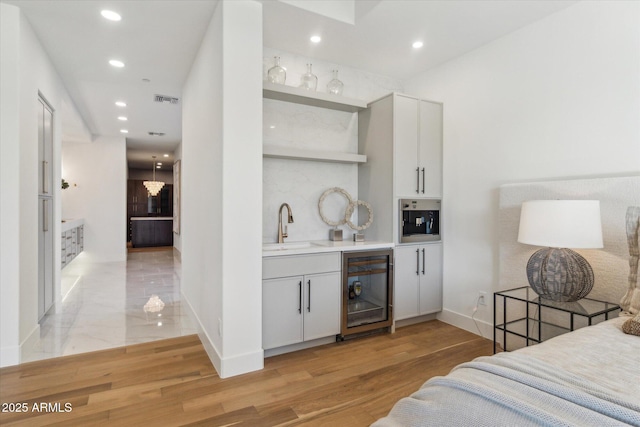 bar with wine cooler, light wood-type flooring, stainless steel oven, sink, and white cabinetry