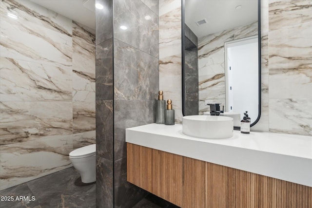 bathroom featuring toilet, vanity, and tile walls