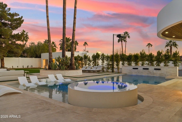 pool at dusk featuring a jacuzzi and a patio area