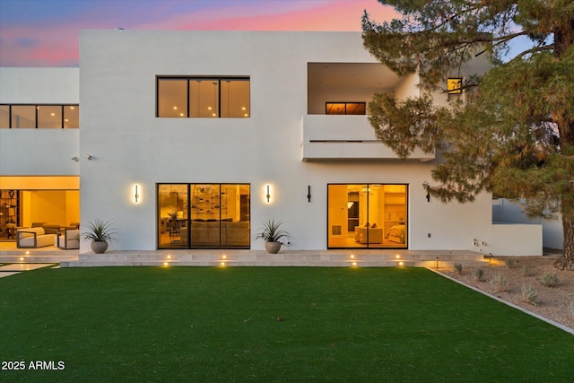 back house at dusk featuring a lawn