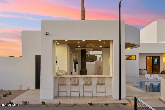 back house at dusk with exterior bar and a patio