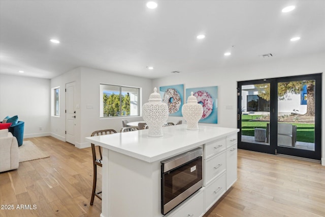 kitchen with a center island, built in microwave, a kitchen bar, white cabinets, and light hardwood / wood-style flooring