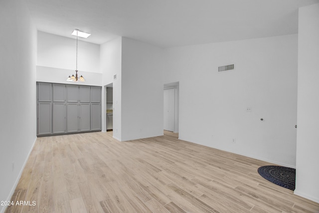 unfurnished living room featuring a notable chandelier, a high ceiling, and light wood-type flooring