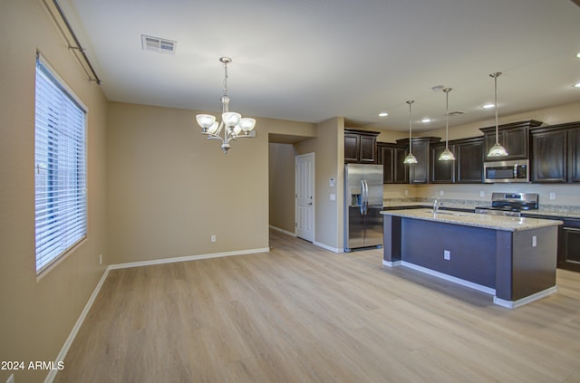 kitchen featuring light wood-type flooring, light stone counters, stainless steel appliances, a kitchen island with sink, and hanging light fixtures