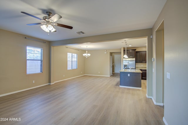 unfurnished living room with ceiling fan with notable chandelier and light hardwood / wood-style flooring