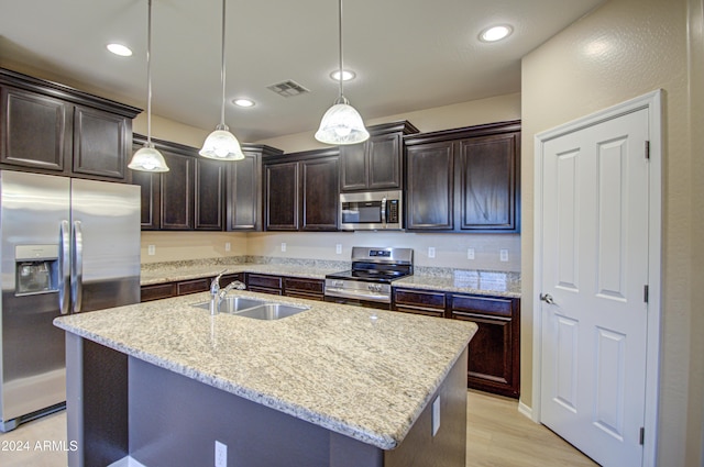 kitchen with decorative light fixtures, light wood-type flooring, an island with sink, and appliances with stainless steel finishes