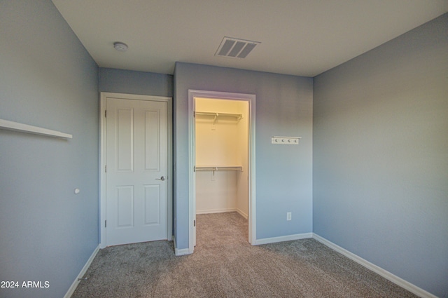 unfurnished bedroom with a walk in closet, light colored carpet, and a closet