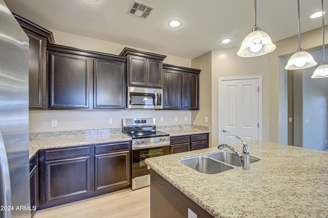 kitchen featuring light stone countertops, sink, pendant lighting, appliances with stainless steel finishes, and light wood-type flooring