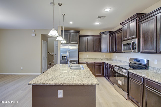 kitchen featuring decorative light fixtures, stainless steel appliances, a kitchen island with sink, and light hardwood / wood-style floors