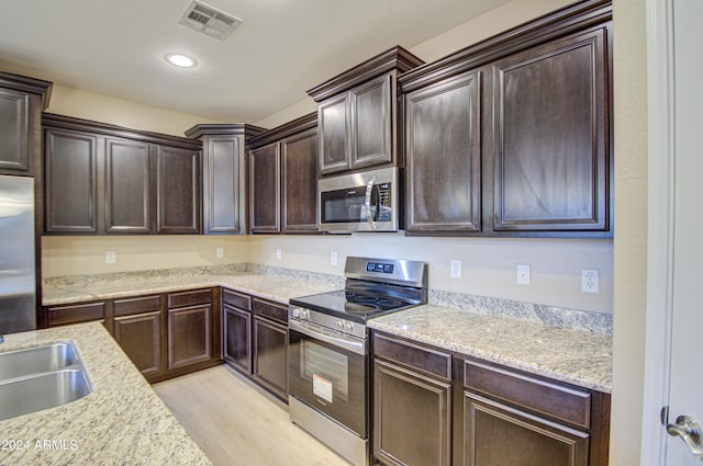 kitchen featuring sink, light stone countertops, appliances with stainless steel finishes, light hardwood / wood-style floors, and dark brown cabinetry