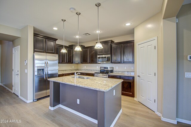 kitchen featuring sink, stainless steel appliances, light hardwood / wood-style flooring, pendant lighting, and a center island with sink