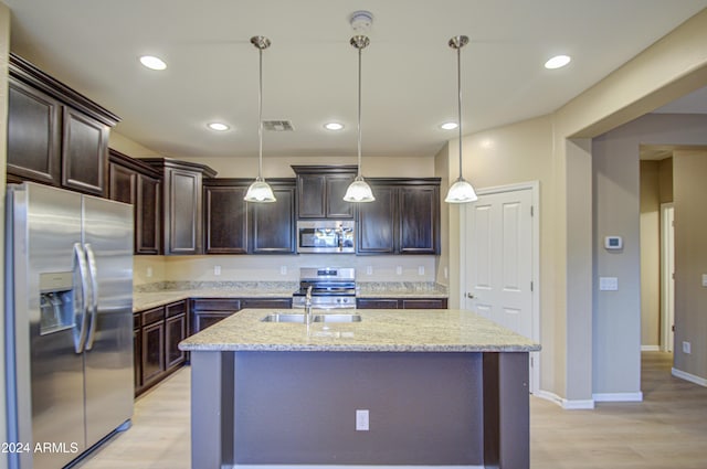 kitchen featuring light stone countertops, appliances with stainless steel finishes, hanging light fixtures, and an island with sink