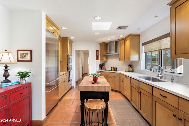 kitchen featuring wall chimney exhaust hood, butcher block countertops, sink, light tile patterned floors, and appliances with stainless steel finishes