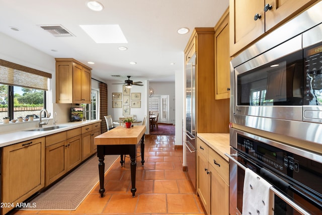 kitchen with a skylight, sink, ceiling fan, built in appliances, and light tile patterned floors