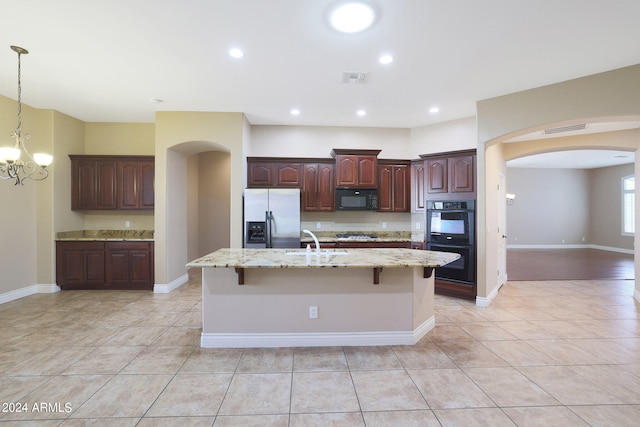 kitchen featuring light tile patterned floors, black appliances, dark brown cabinets, a center island with sink, and a notable chandelier