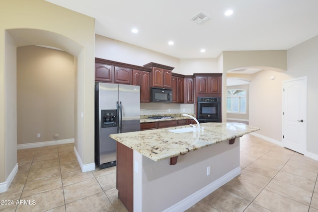 kitchen featuring black appliances, light tile patterned flooring, a kitchen island with sink, and a breakfast bar area