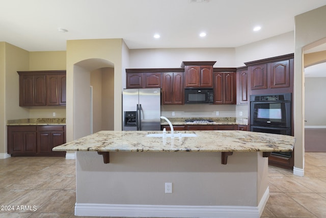 kitchen with a kitchen breakfast bar, black appliances, a kitchen island with sink, and sink