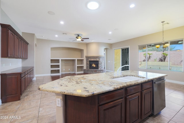 kitchen featuring light tile patterned floors, decorative light fixtures, a kitchen island with sink, a fireplace, and ceiling fan with notable chandelier