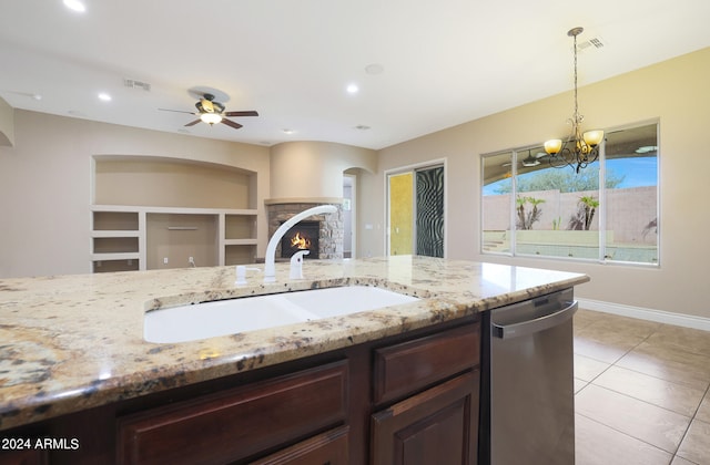 kitchen featuring ceiling fan with notable chandelier, a stone fireplace, dishwasher, decorative light fixtures, and sink