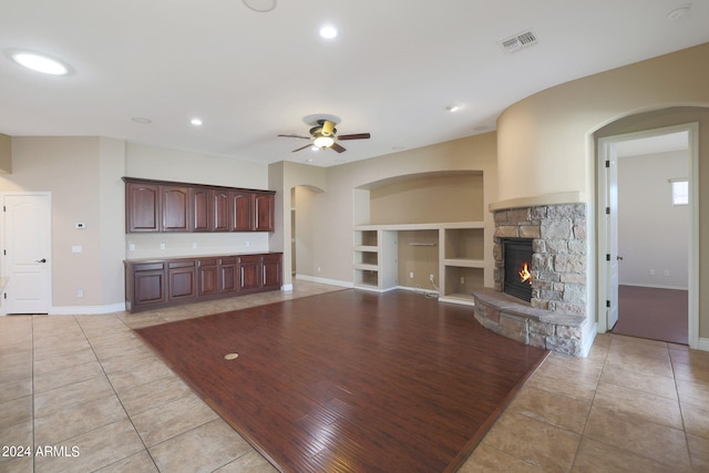 unfurnished living room with ceiling fan, light tile patterned flooring, a fireplace, and built in features