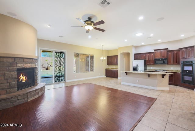 kitchen with ceiling fan, a stone fireplace, black appliances, a breakfast bar area, and light hardwood / wood-style floors