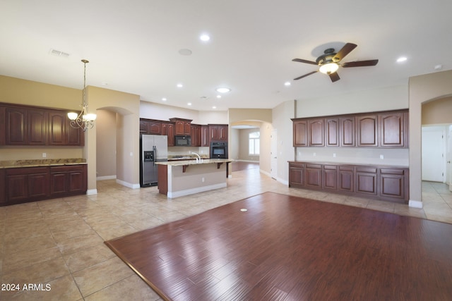 kitchen featuring hanging light fixtures, light hardwood / wood-style floors, ceiling fan with notable chandelier, black appliances, and a center island with sink