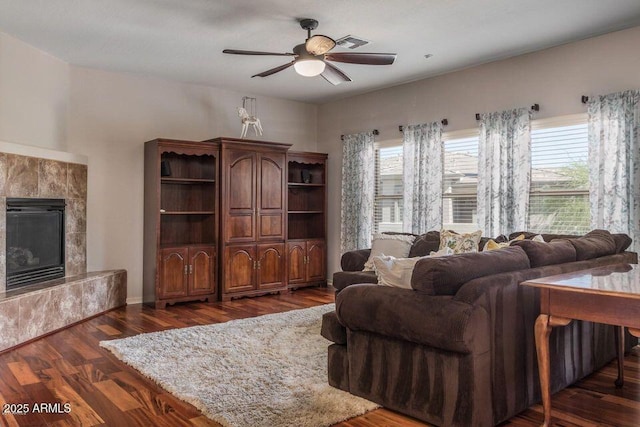 living room with ceiling fan, dark wood-type flooring, a tiled fireplace, and plenty of natural light