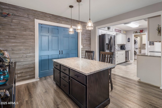 kitchen featuring dark brown cabinetry, white cabinets, stainless steel refrigerator with ice dispenser, stacked washer and clothes dryer, and pendant lighting