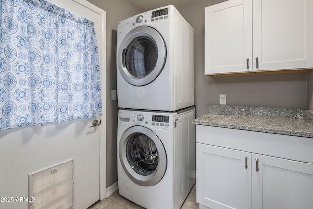 laundry room with light tile patterned floors, stacked washing maching and dryer, and cabinet space