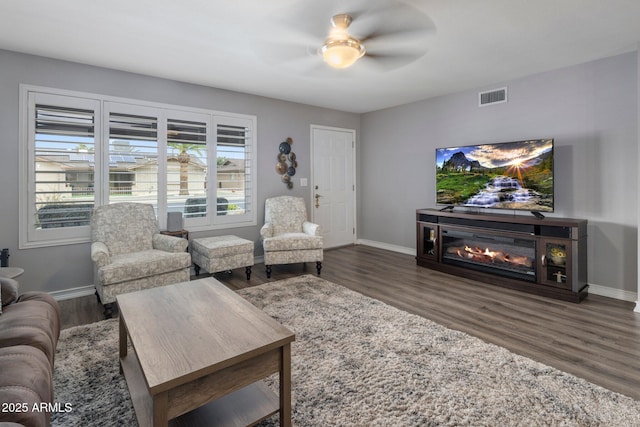 living area featuring dark wood-type flooring, a glass covered fireplace, visible vents, and baseboards