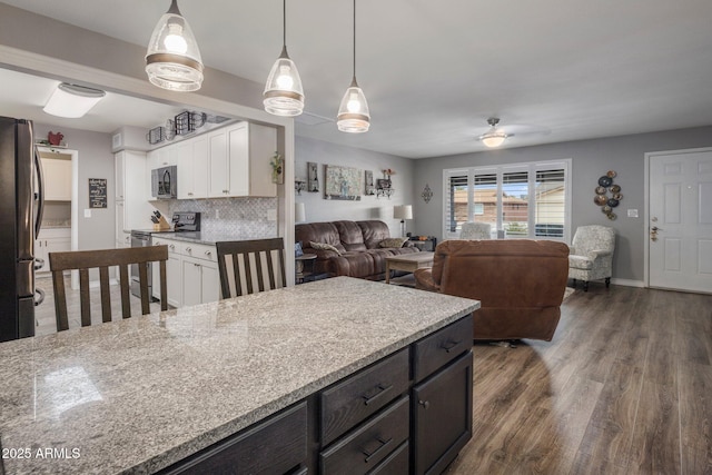 kitchen featuring light stone counters, white cabinetry, open floor plan, appliances with stainless steel finishes, and decorative light fixtures