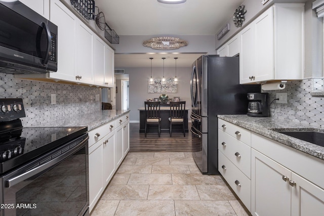 kitchen featuring light stone counters, hanging light fixtures, black / electric stove, white cabinetry, and backsplash