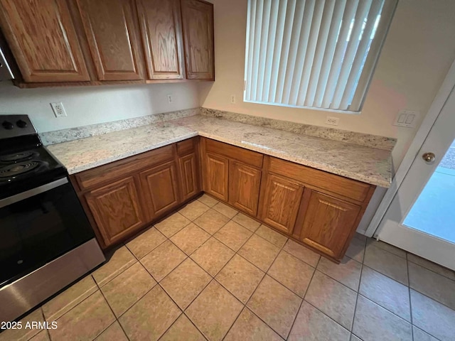 kitchen with light tile patterned floors, stainless steel range with electric cooktop, and light stone counters