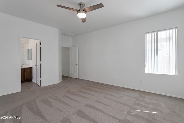 unfurnished bedroom featuring ceiling fan, ensuite bath, and light carpet