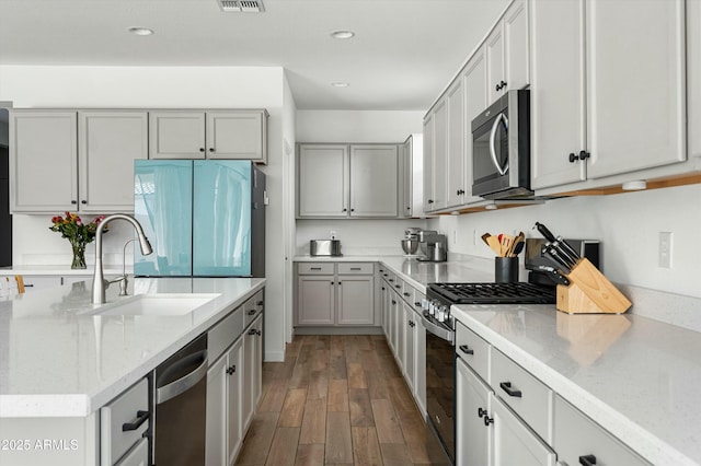 kitchen featuring sink, dark hardwood / wood-style floors, gray cabinets, appliances with stainless steel finishes, and light stone counters