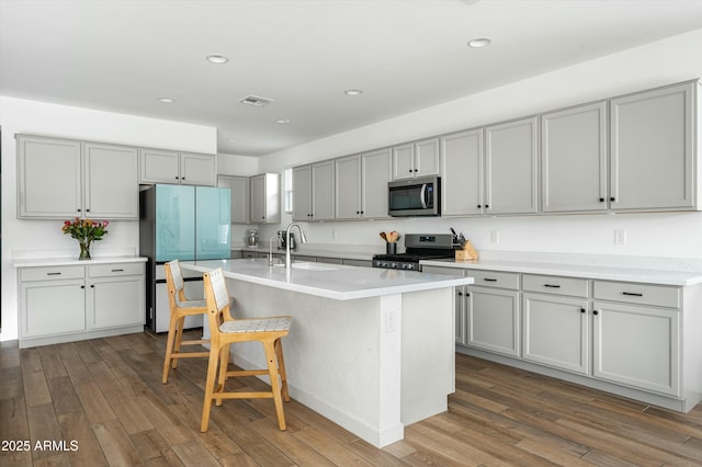 kitchen featuring gray cabinetry, dark hardwood / wood-style floors, an island with sink, a breakfast bar area, and appliances with stainless steel finishes