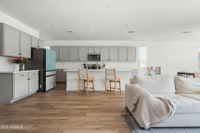 kitchen with a kitchen breakfast bar, stainless steel appliances, a kitchen island with sink, and gray cabinetry