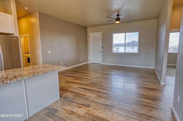 interior space featuring wood-type flooring, light stone counters, white cabinets, ceiling fan, and stainless steel fridge