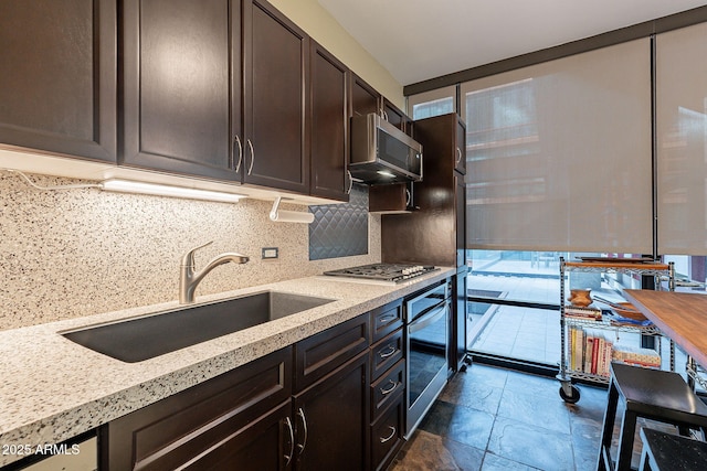 kitchen featuring sink, appliances with stainless steel finishes, tasteful backsplash, light stone counters, and dark brown cabinetry