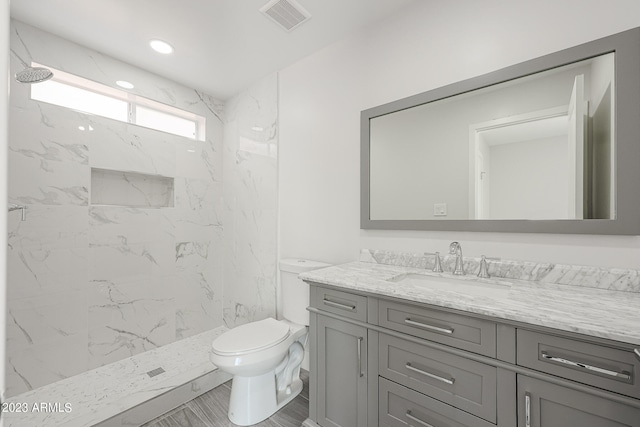 bathroom featuring toilet, a tile shower, and vanity