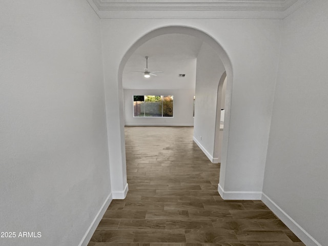 hallway featuring ornamental molding, arched walkways, dark wood-style flooring, and baseboards