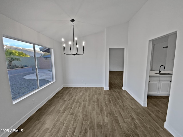 unfurnished dining area with a notable chandelier, lofted ceiling, a sink, wood finished floors, and baseboards