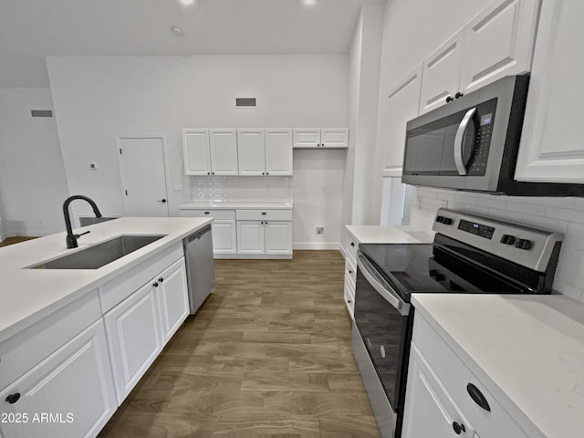 kitchen with light countertops, decorative backsplash, appliances with stainless steel finishes, white cabinets, and a sink