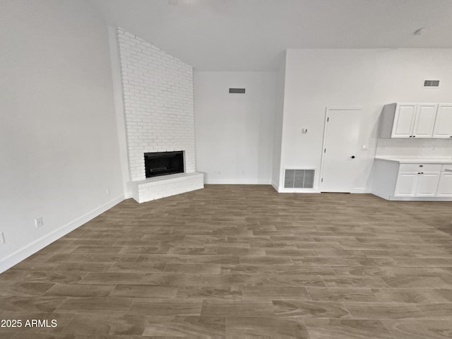 unfurnished living room featuring visible vents, a fireplace, baseboards, and wood finished floors