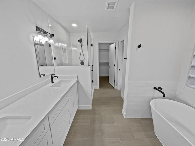 full bathroom featuring a sink, visible vents, a spacious closet, a soaking tub, and double vanity