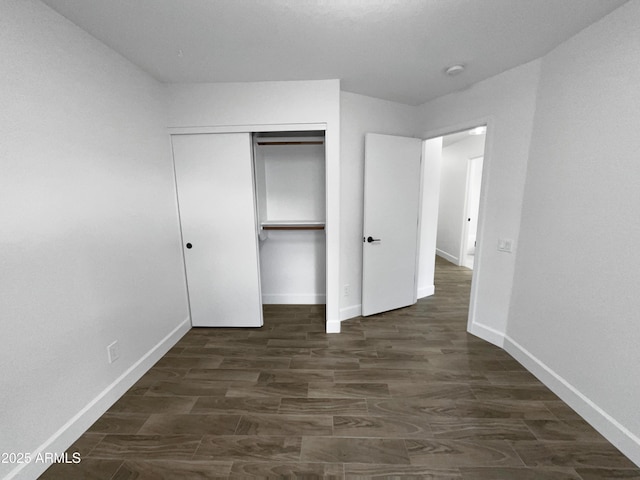 unfurnished bedroom featuring dark wood-style floors, a closet, and baseboards