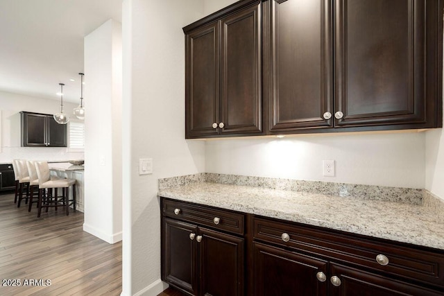 kitchen featuring wood-type flooring, light stone countertops, dark brown cabinets, and pendant lighting