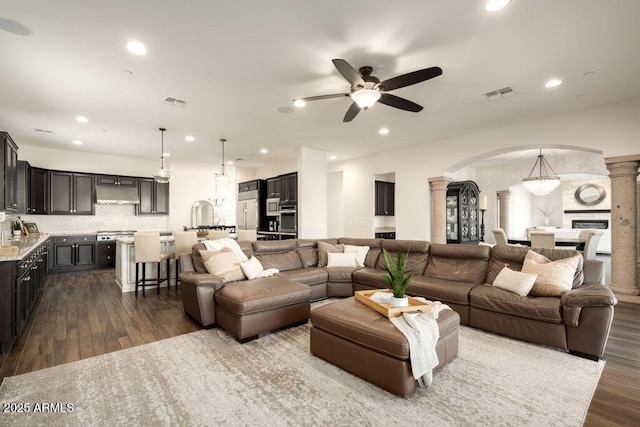 living room with decorative columns, sink, dark wood-type flooring, and ceiling fan with notable chandelier