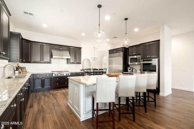 kitchen featuring sink, a breakfast bar, hanging light fixtures, a center island, and built in appliances