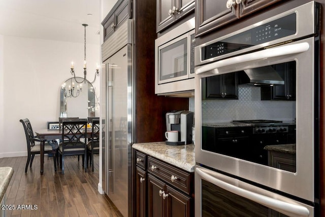 kitchen featuring dark brown cabinetry, built in appliances, hanging light fixtures, dark hardwood / wood-style floors, and decorative backsplash
